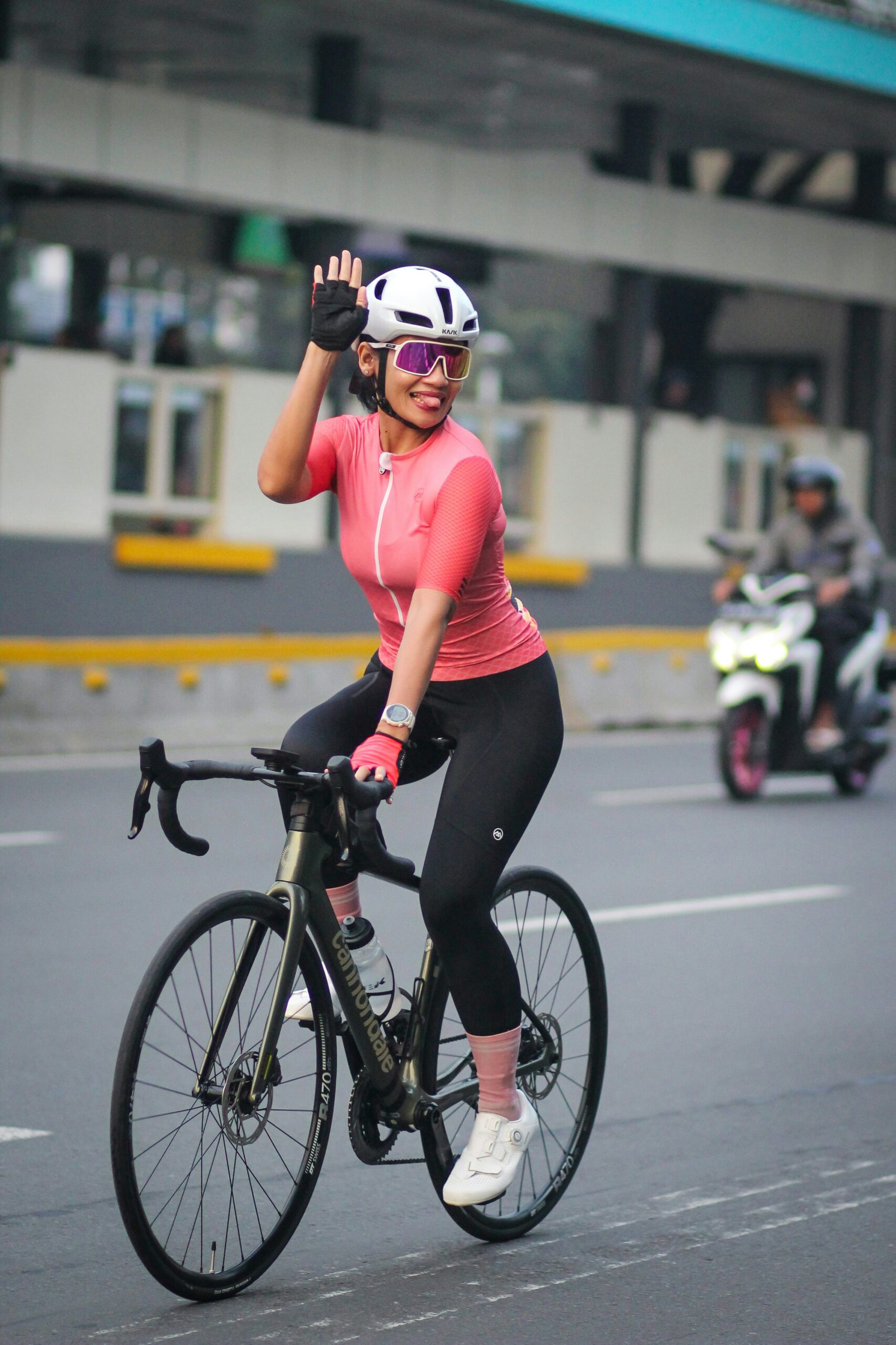 A girl waving her hand to other person while cycling.
